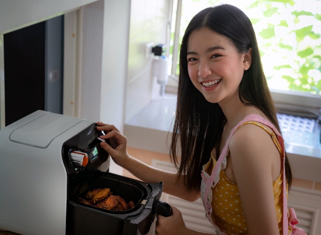 Asian girl cooking a fried chicken by Air Fryer machine in her kitchen