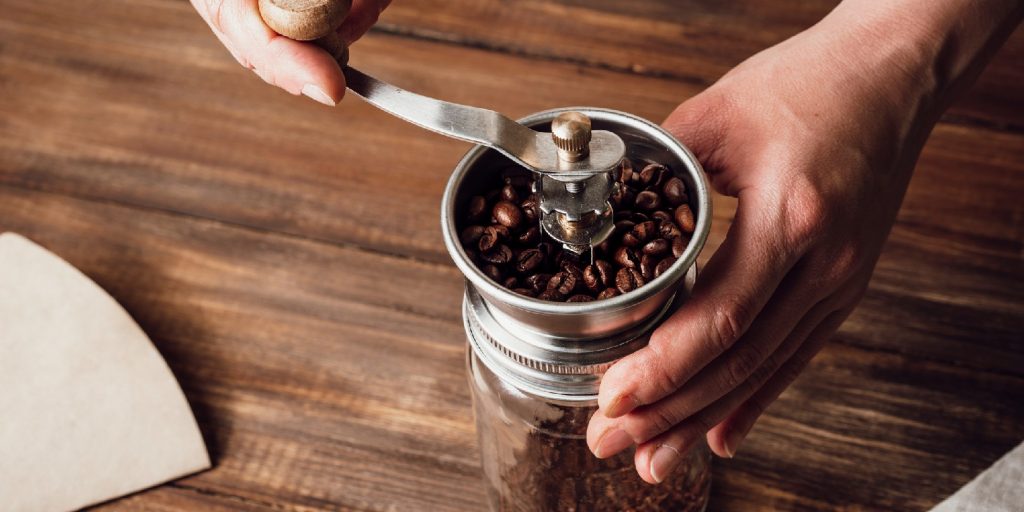 Grinding coffee beans in a manual coffee grinder on a wooden table