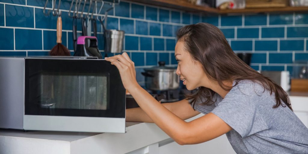 Side shot of a beautiful Asian woman opening her microwave to checking her meals that reheated.