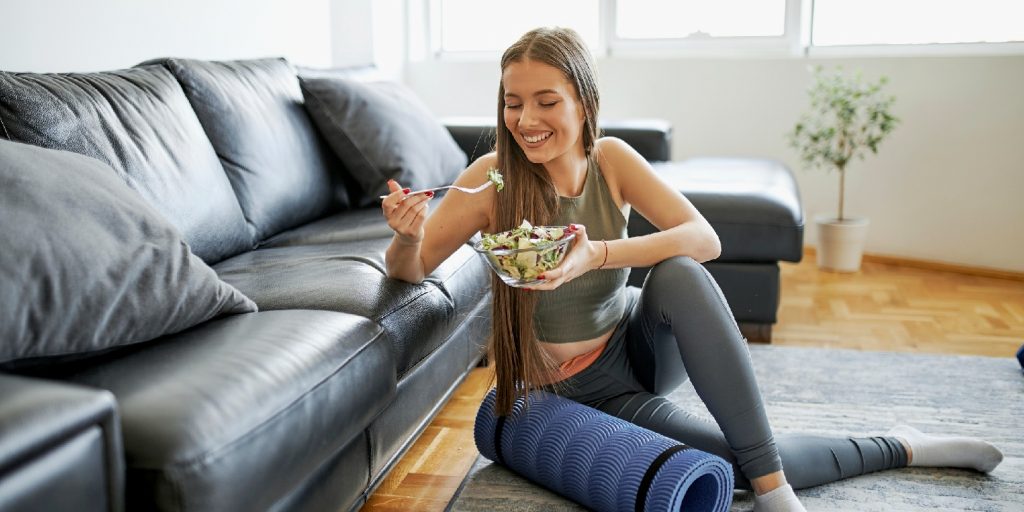 Beautiful woman eating fresh salad after intensive home workout