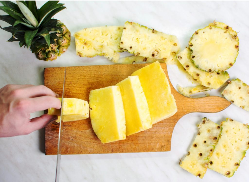 Person slicing pineapple on a cutting board