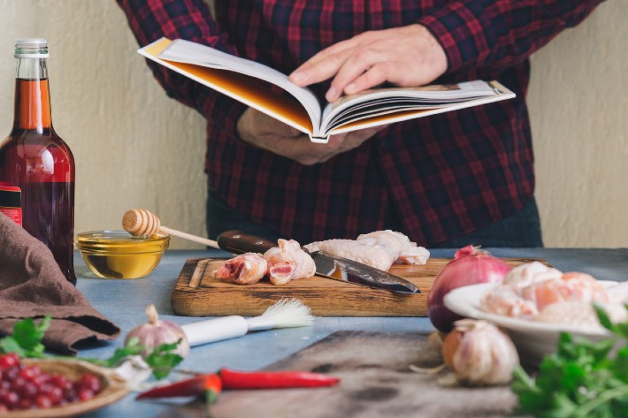 A person reading a recipe in their camping cookbook to prepare a meal.