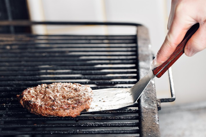A man about to turn a burger patty on a hot grill using a griddle spatula, demonstrating the use of the best griddle spatula for cooking.